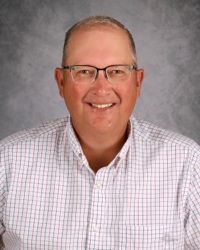 Smiling man in glasses and checkered shirt against a gray studio backdrop