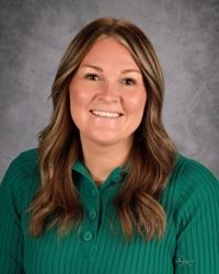 Smiling person in a green sweater against a gray studio backdrop