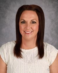Portrait of a smiling woman with dark hair against a gray studio backdrop, wearing a white blouse