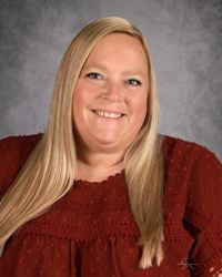 Smiling woman with long blonde hair in a red top against a gray studio backdrop