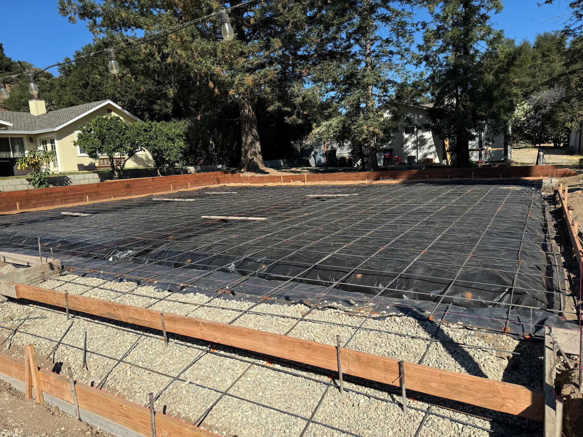Concrete foundation under construction with rebar grid and wooden forms in a residential yard