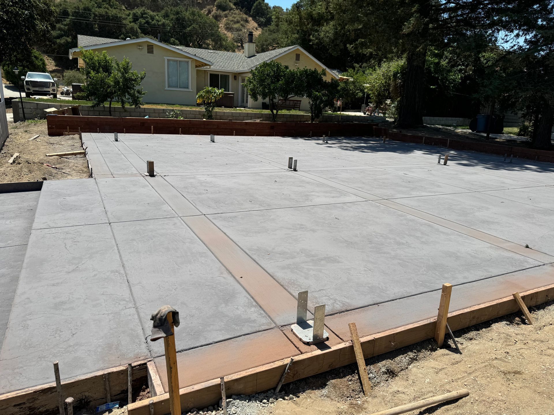 Concrete foundation slab under construction in a yard, with wooden forms and a house in the background