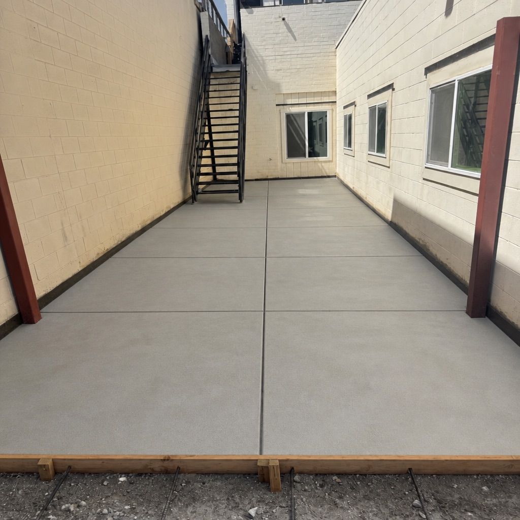 Empty concrete courtyard beside a beige building, with exterior stairs and windows.