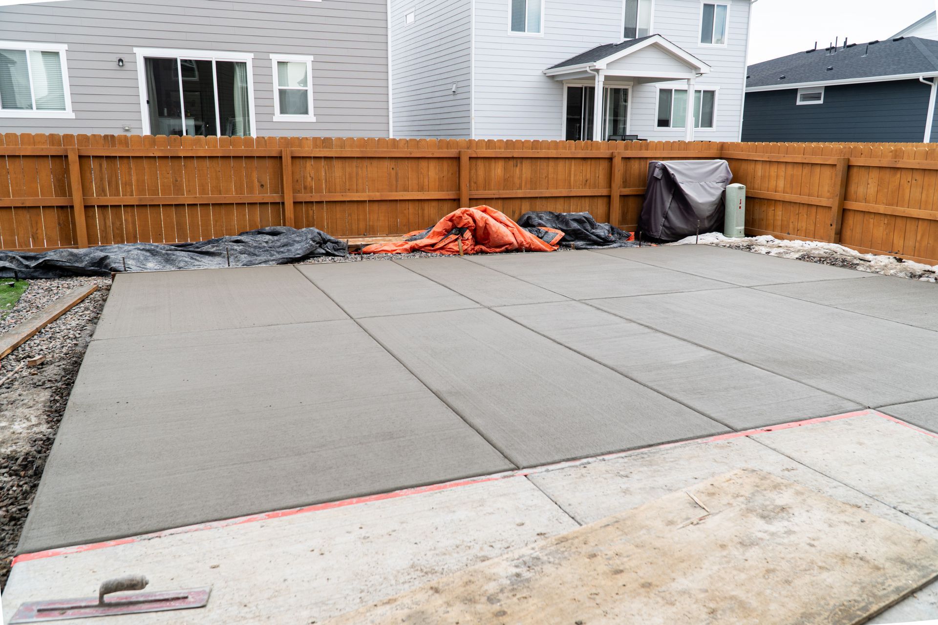 New concrete patio slab in a fenced backyard, with construction materials along the back edge.