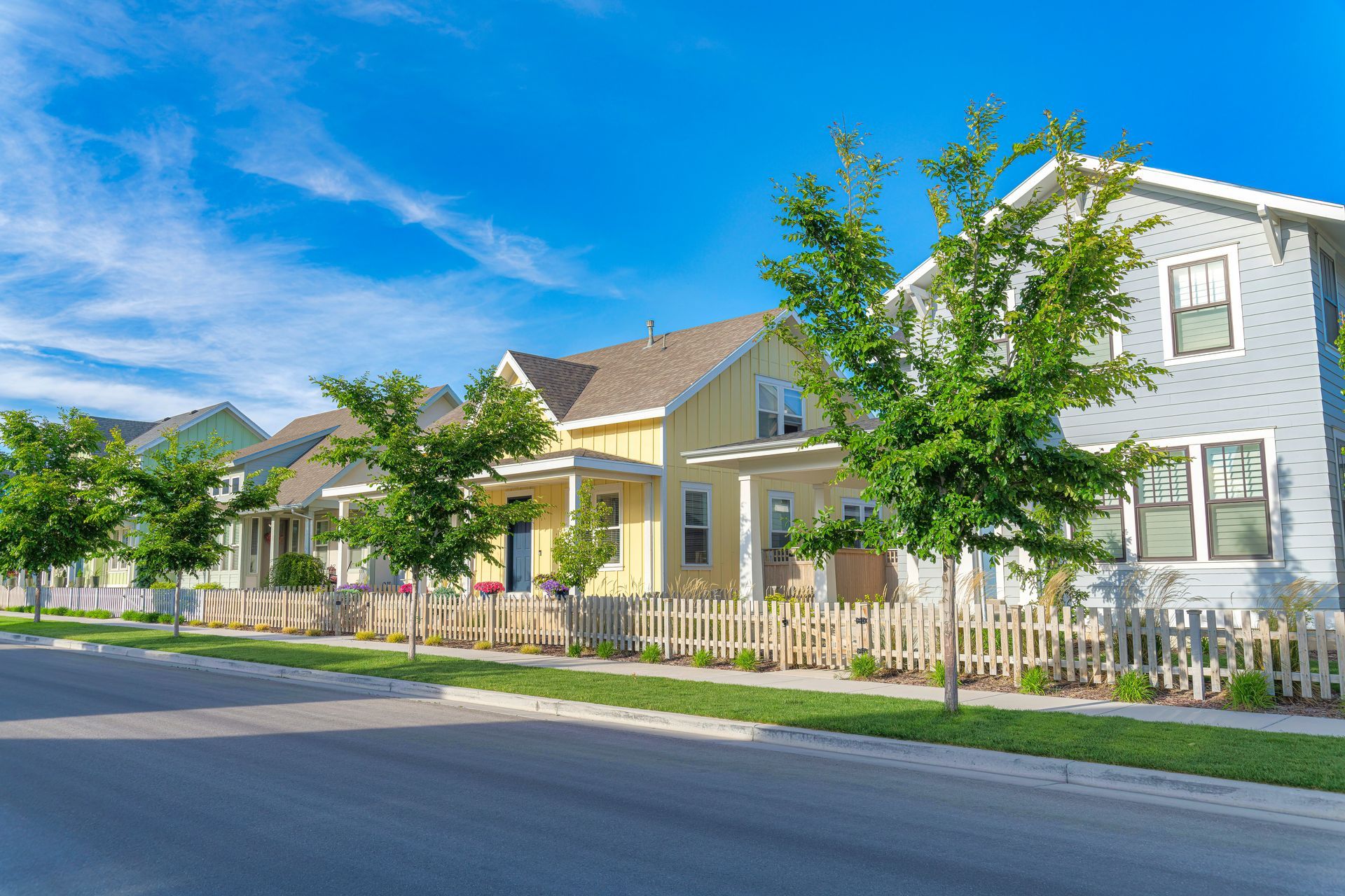 Suburban street with colorful houses, picket fences, and trees under a bright blue sky