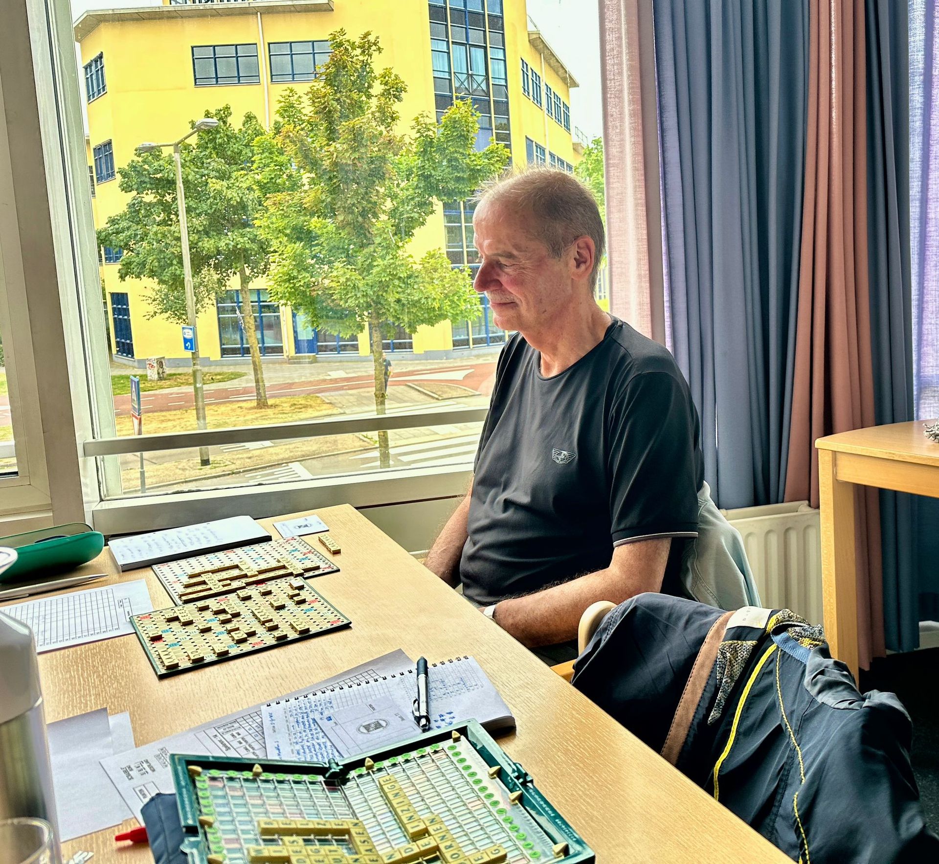 Een man zit aan een tafel en kijkt uit het raam. Op de tafel liggen papieren en printplaten.