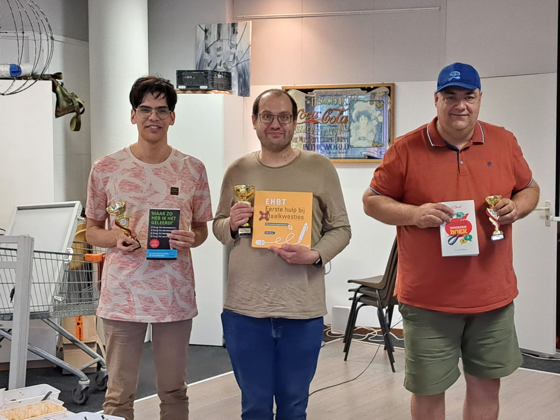 Drie mensen met prijzen en boeken staan ​​voor een witte muur.