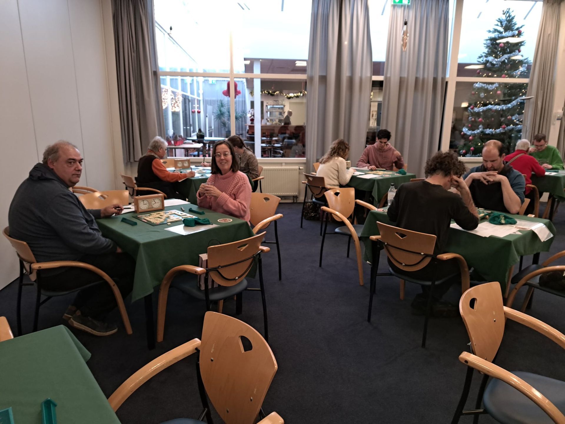 Mensen spelen spelletjes aan tafels in een felverlichte ruimte met ramen.