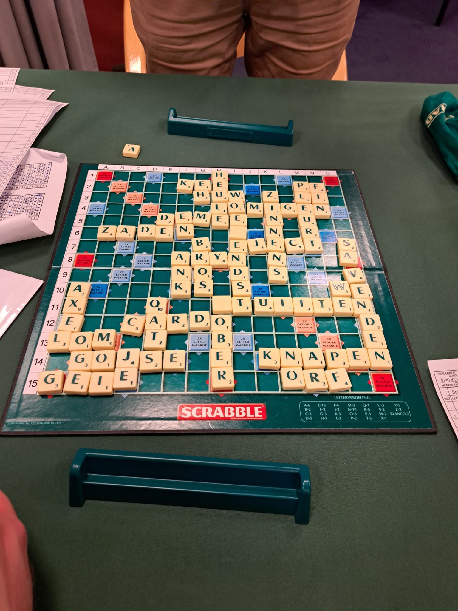 Een Scrabble-spel wordt gespeeld op een groene tafel, waarbij de lettertegels en houders zichtbaar zijn.