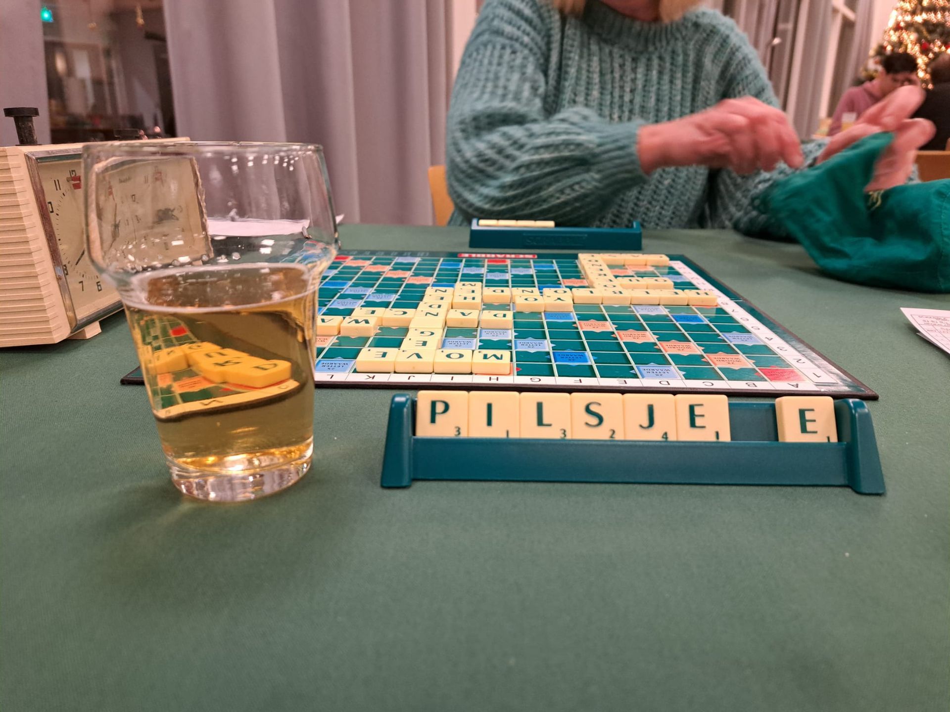 Een Scrabble-spel in volle gang, met een bierglas op de voorgrond en een speler op de achtergrond.