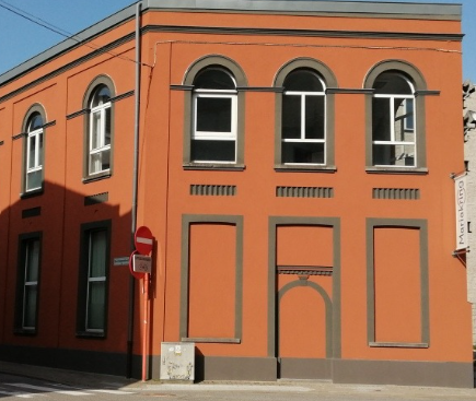 Oranje gebouw met boogvensters, donkere kozijnen en een gesloten deur.