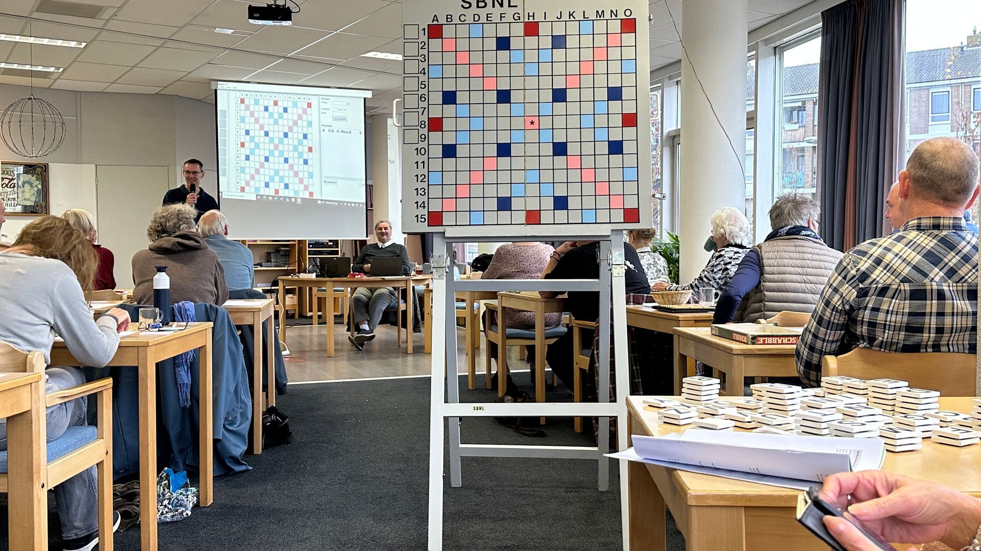 Mensen spelen een bordspel in een kamer, met een groot speelbord op een standaard in het midden.