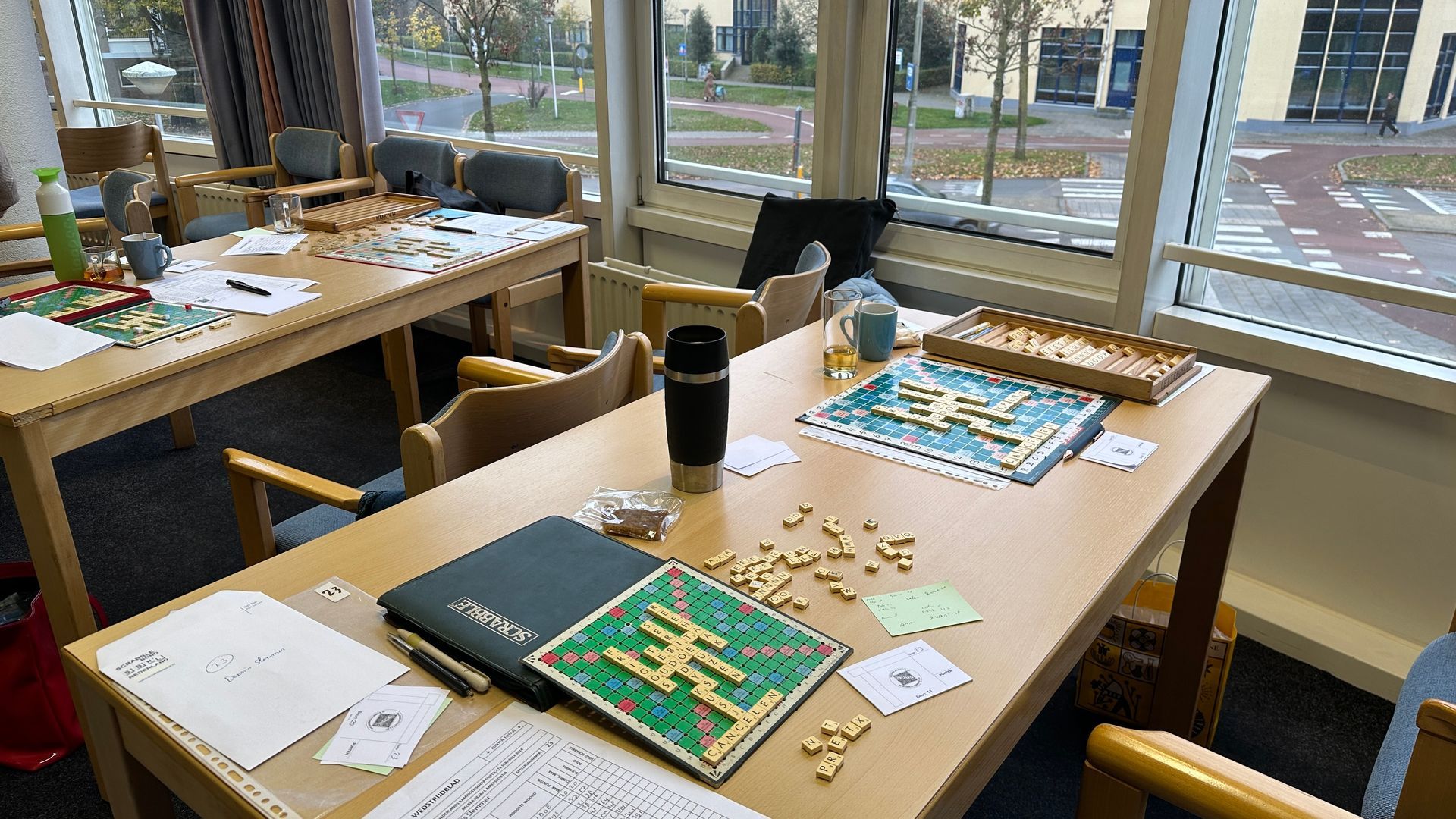 Tafels met bordspellen en kopjes, bij een raam. Zonlicht, binnenomgeving.