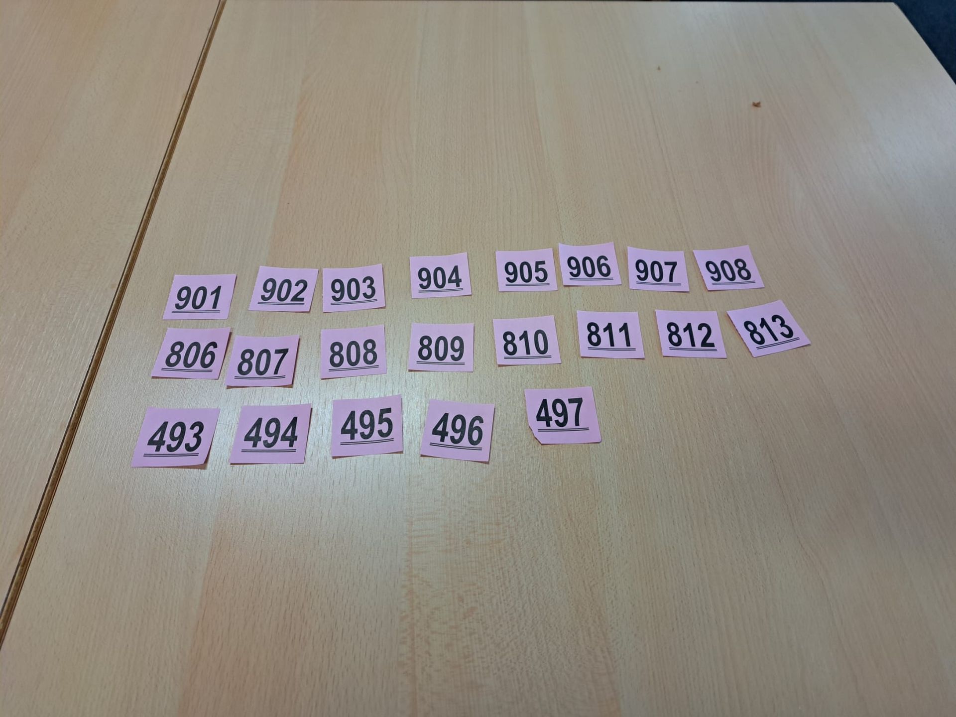 Roze plakbriefjes met zwarte nummers: 901-908, 806-813, 493-497, gerangschikt op een licht houten oppervlak.