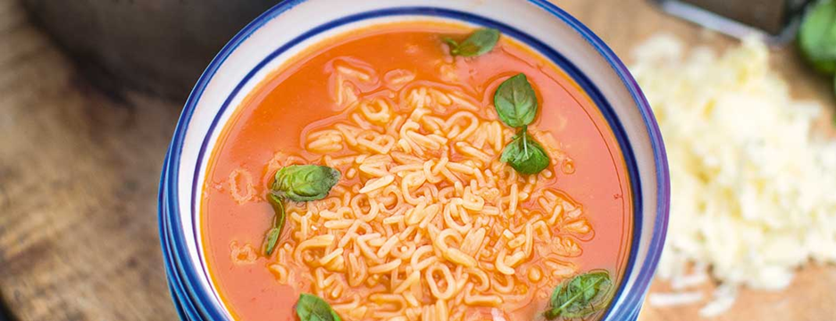 Een kom tomatensoep met noedels, basilicum en geraspte kaas.