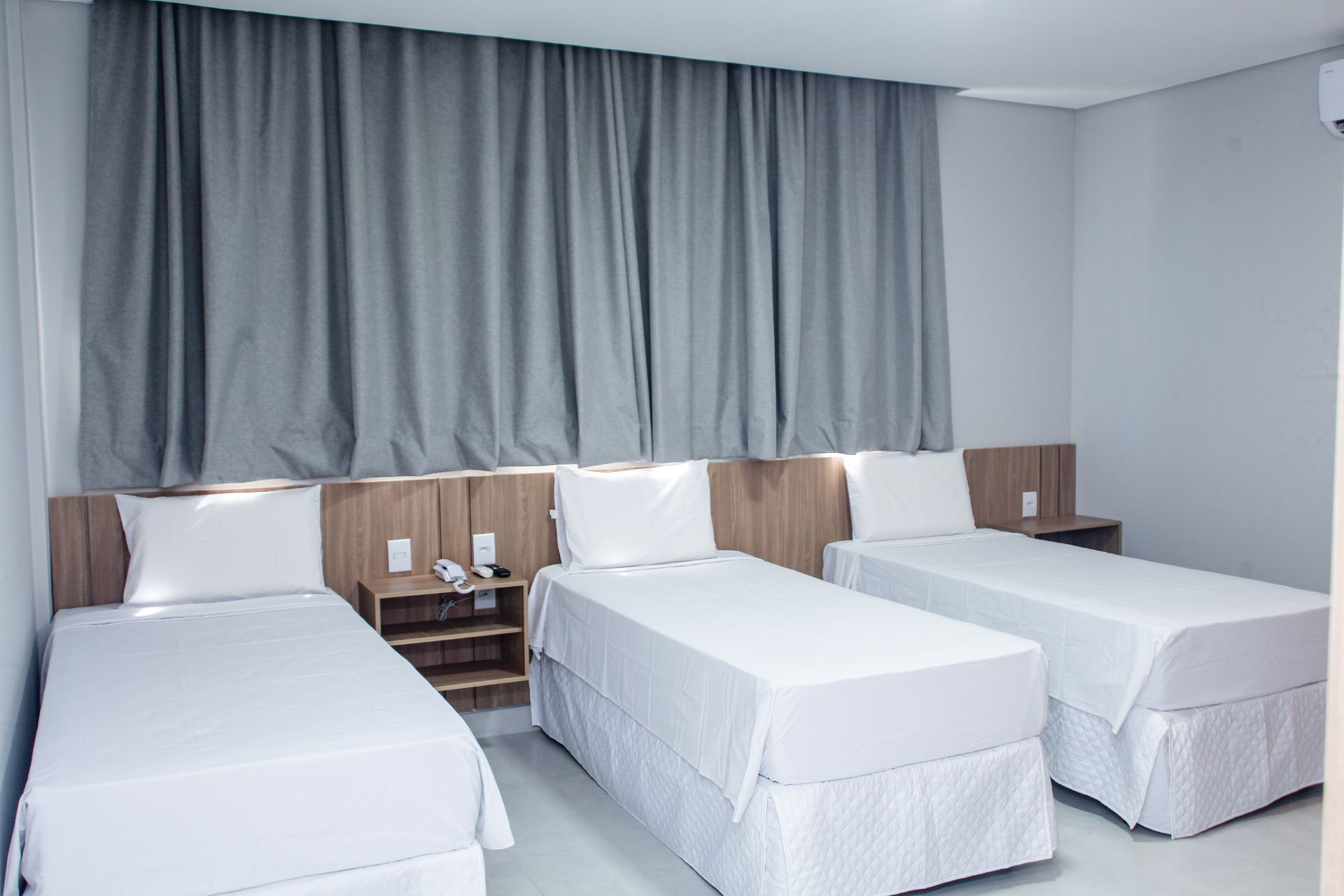 Um quarto de hotel com três camas e cortinas cinzas. Hotel Solar Paulista