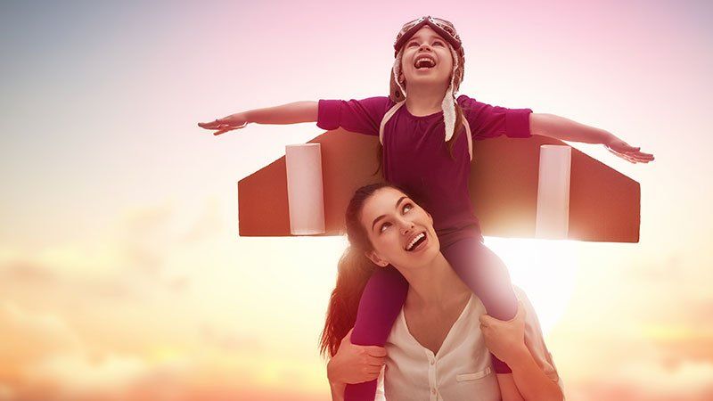 child wearing wings sits on a woman's shoulders