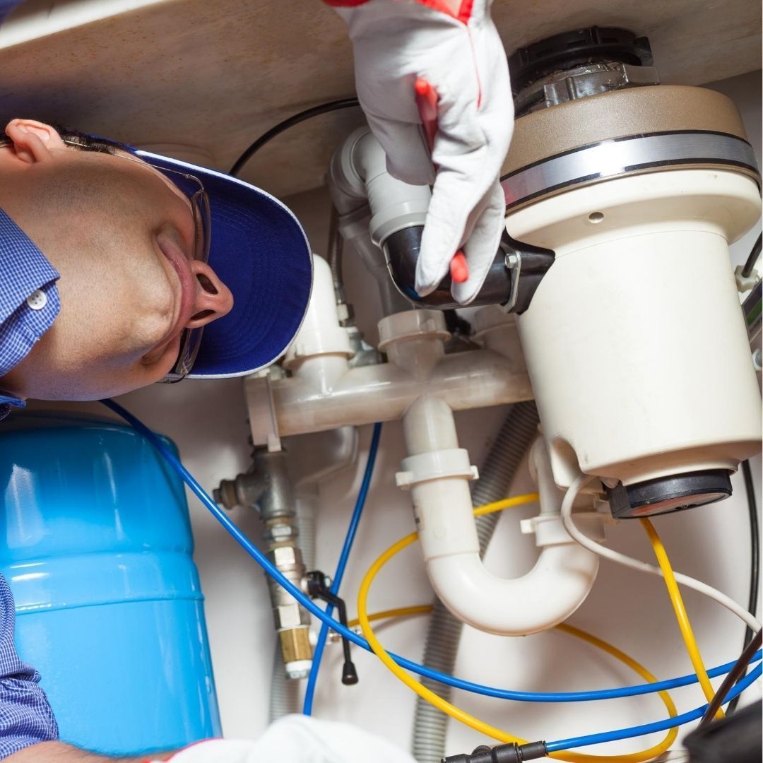 A Man is Fixing a Garbage Disposal in a Kitchen — Wigg Plumbing in Palmerston, NT