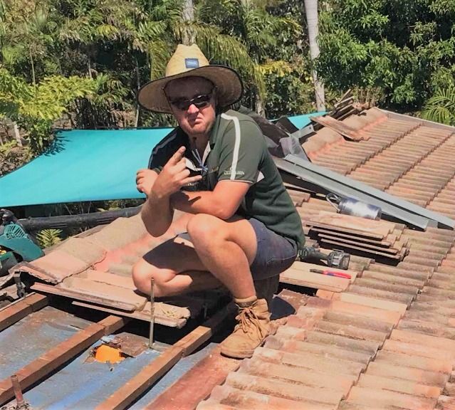 A Man Wearing a Cowboy Hat is Squatting on a Roof — Wigg Plumbing in Berrimah, NT