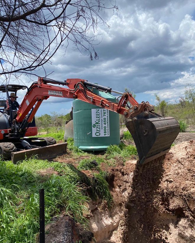 An Excavator is Digging a Hole in the Ground Next to a Green Tank — Wigg Plumbing in Nightcliff, NT