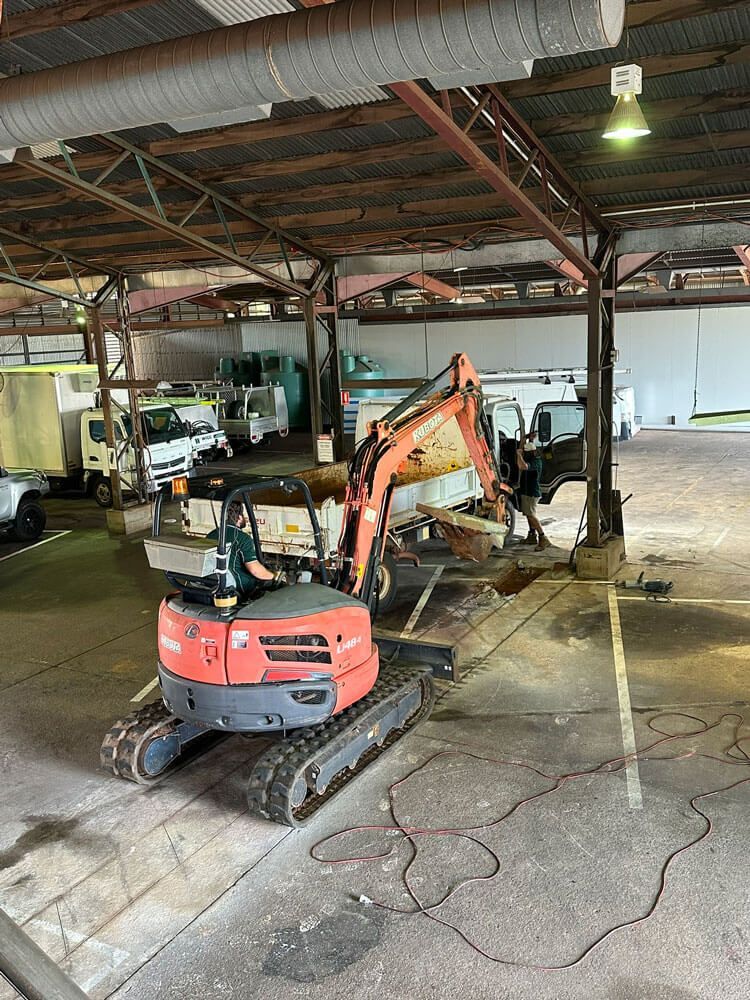 A Man is Driving a Small Excavator in a Warehouse — Wigg Plumbing in Berrimah, NT