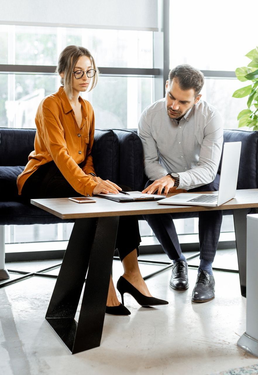 A man and a woman are sitting at a table looking at a laptop.