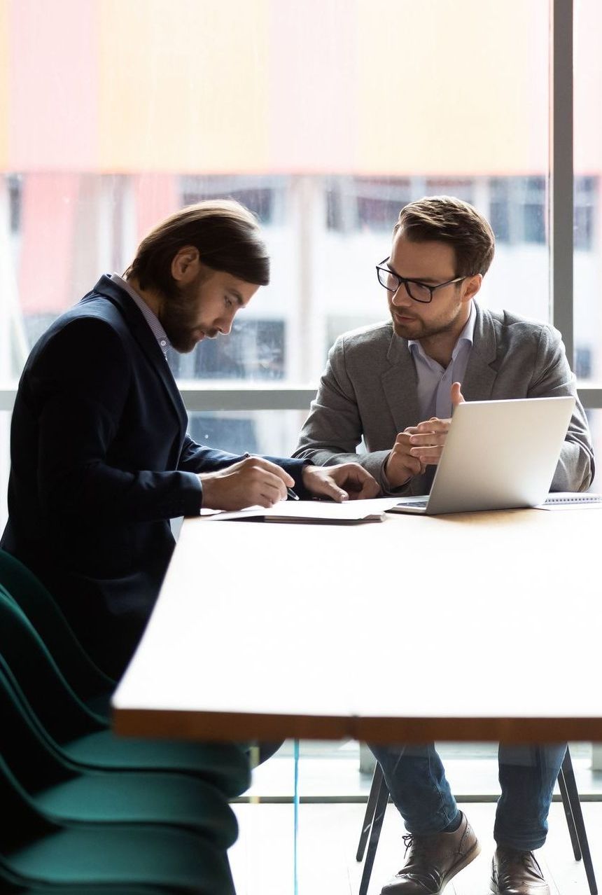 Two men are sitting at a table with a laptop.
