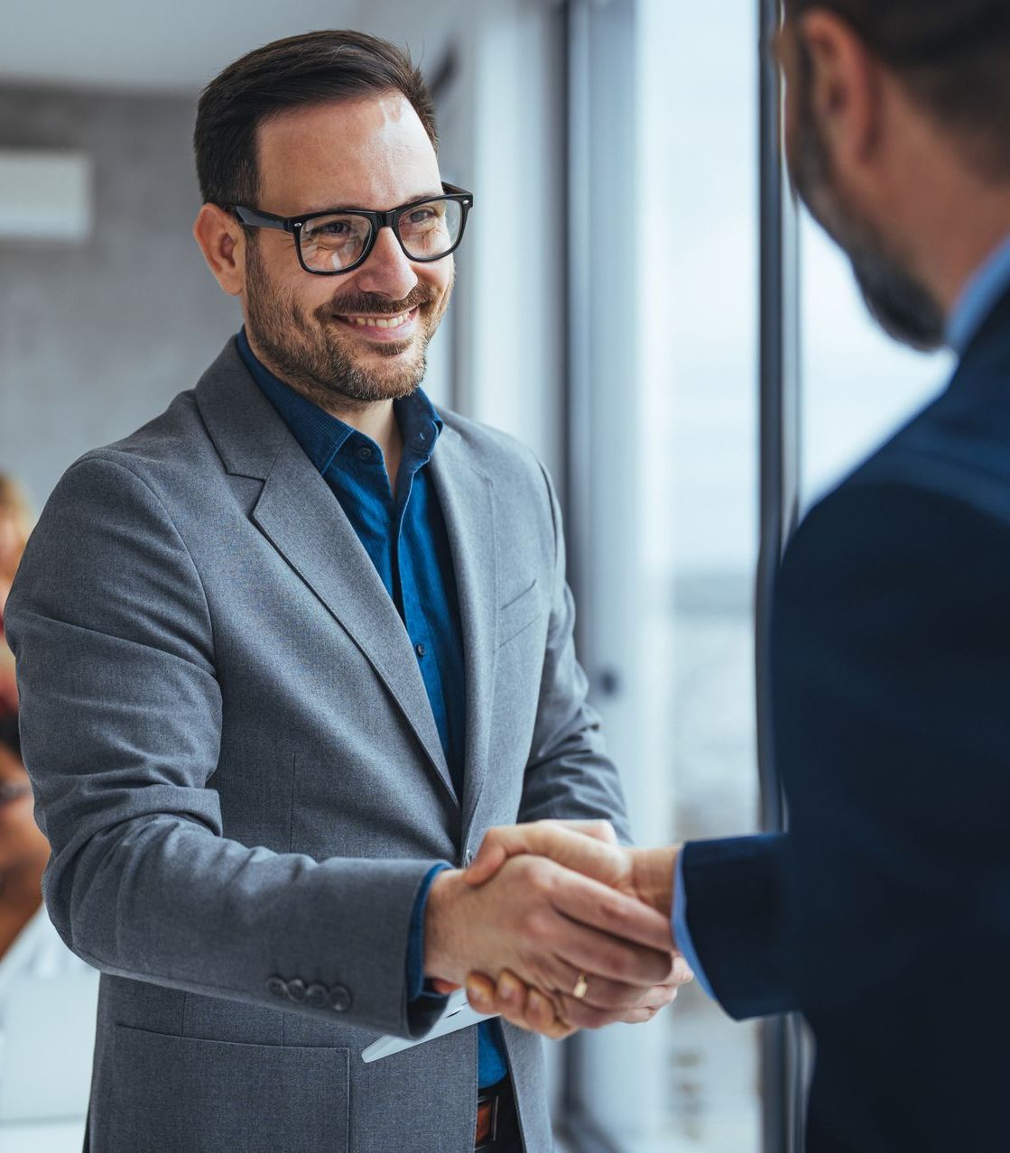 A man in a suit and glasses shakes hands with another man.
