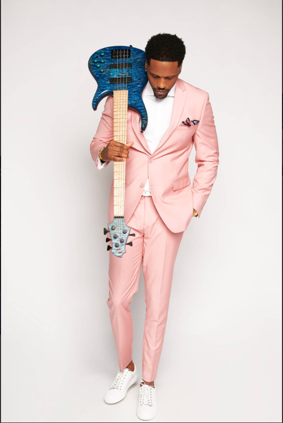 Man in a pink suit holding a blue electric guitar against a white background