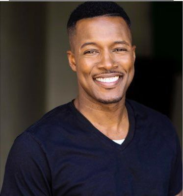 Smiling man in a dark V-neck shirt against a blurred background.