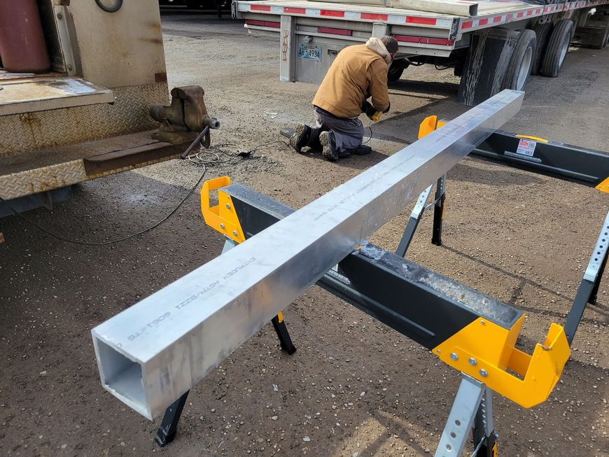 A man is kneeling down next to a large piece of metal