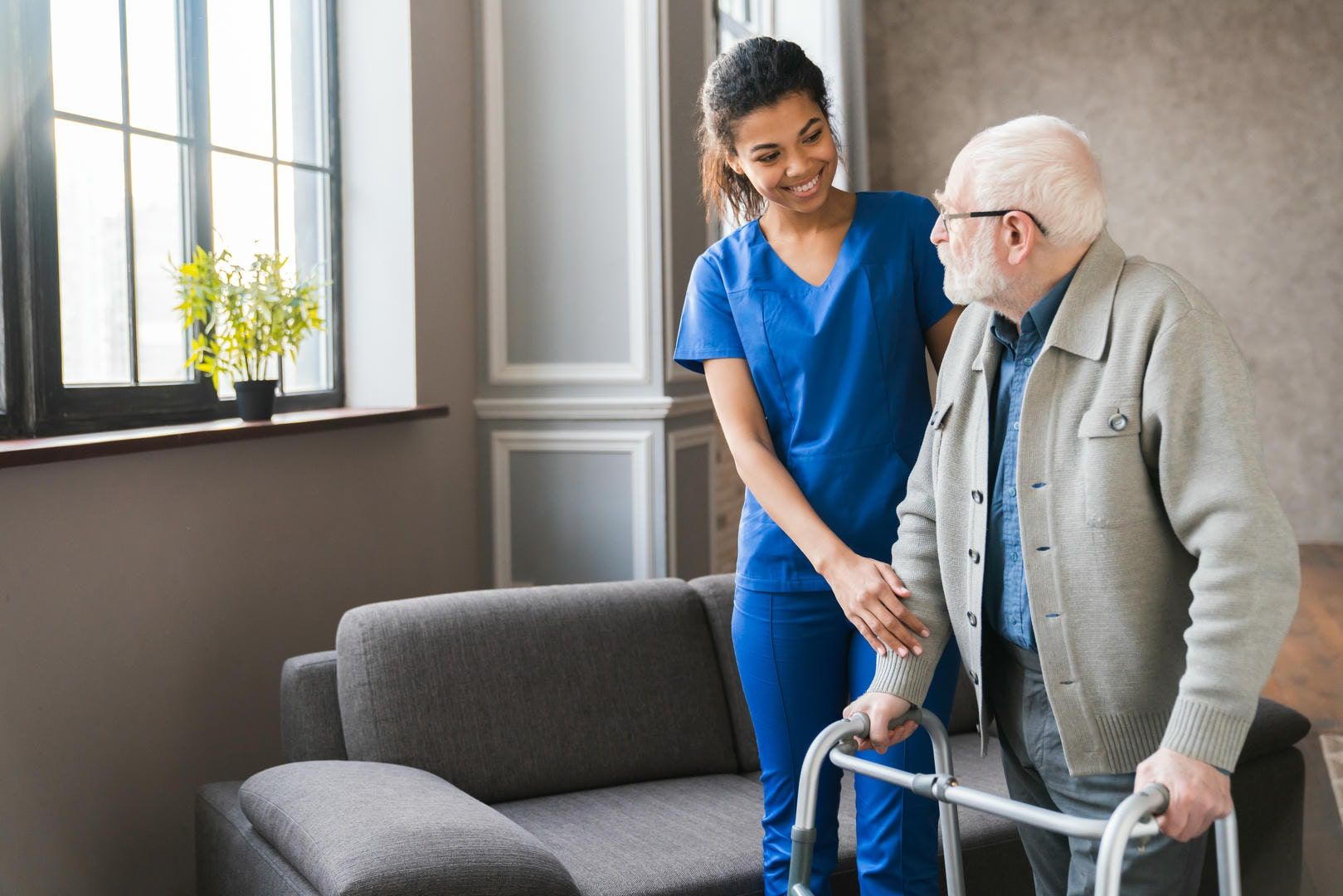 Caregiver assisting an elderly man using a walker indoors.