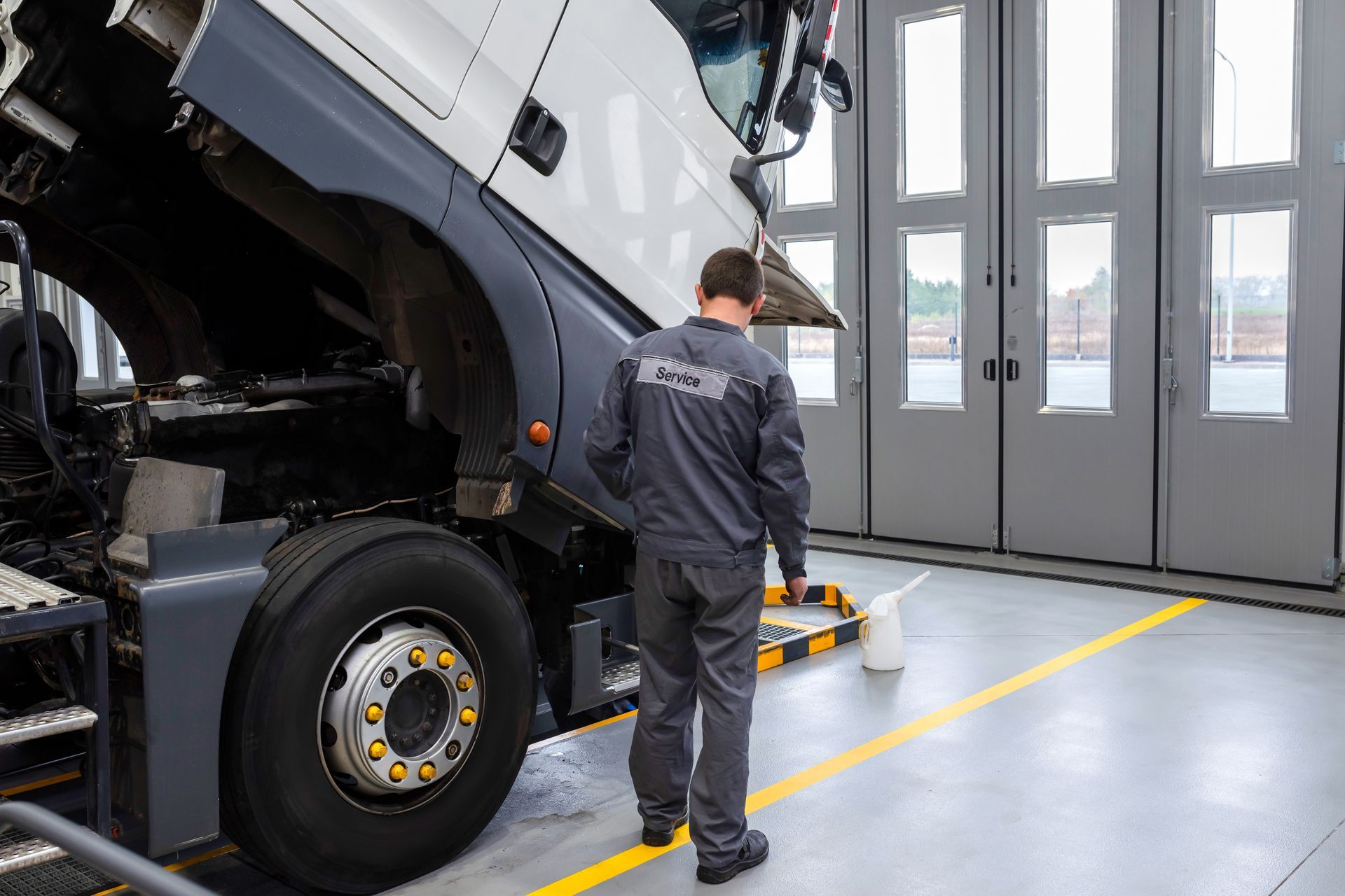 Mechanic inspecting a truck engine with the hood open in a service bay.