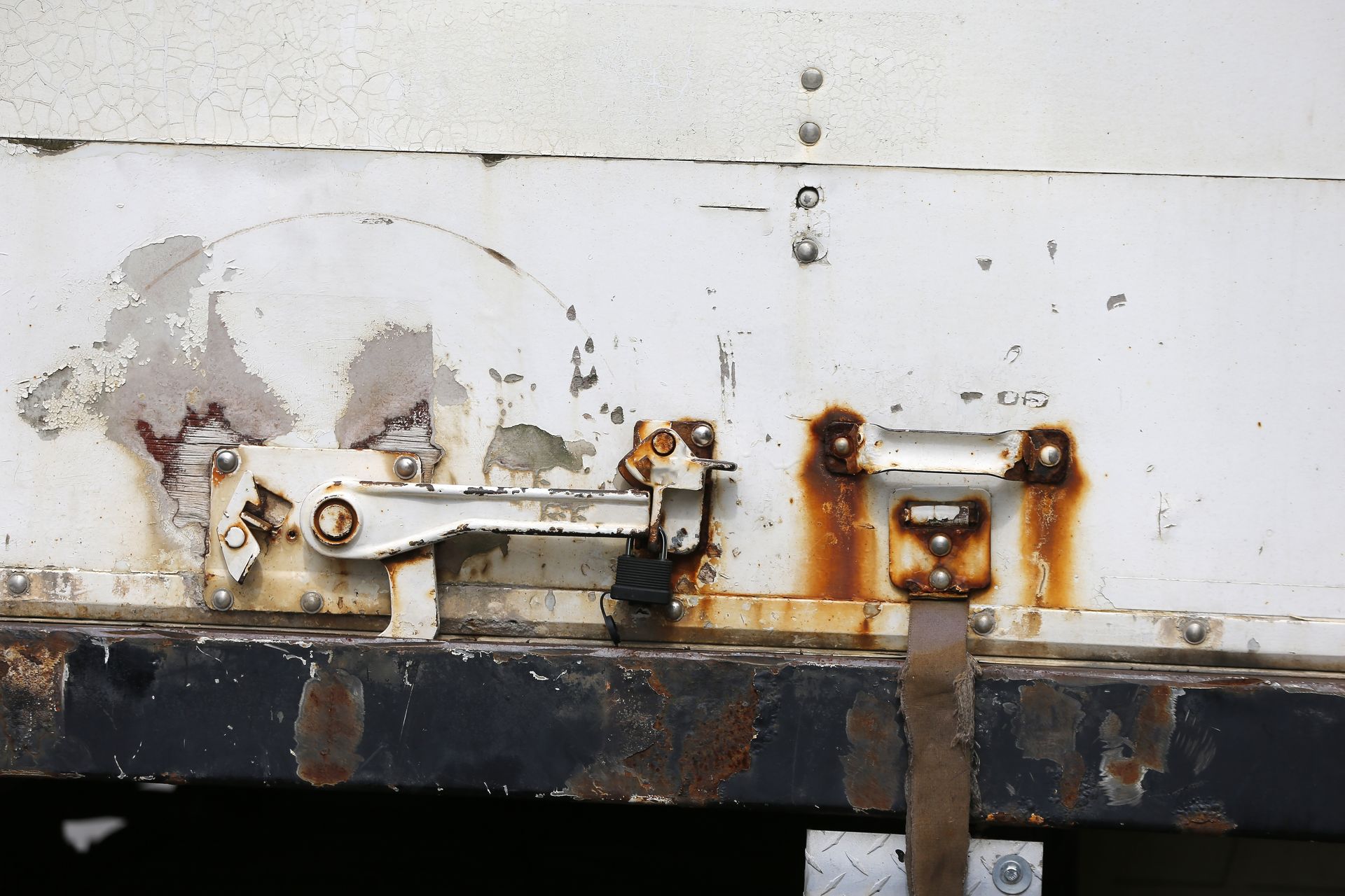 Rusting metal latch and trim on a weathered white truck body.