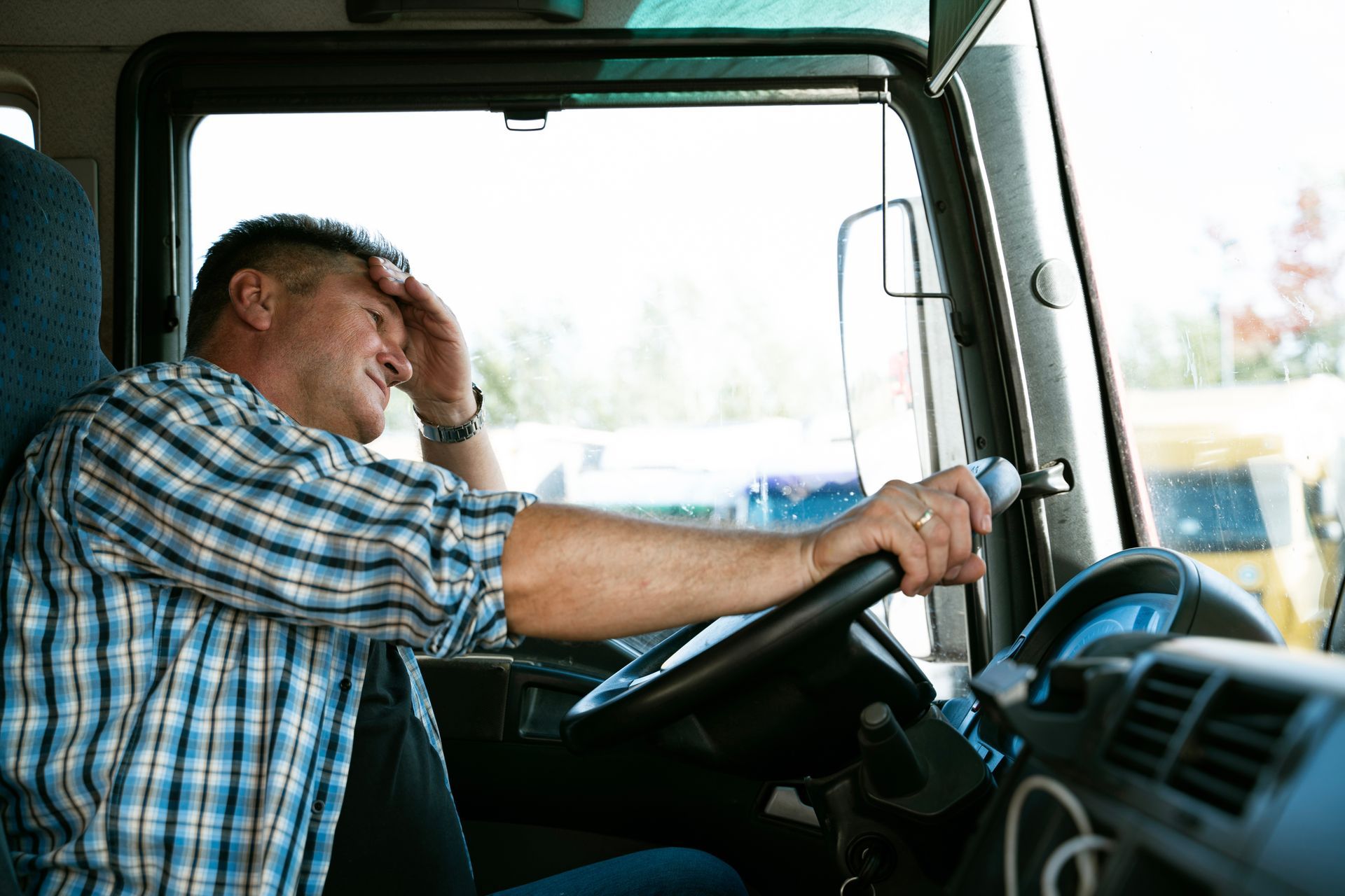Driver with hand on forehead, stressed, in truck cab.