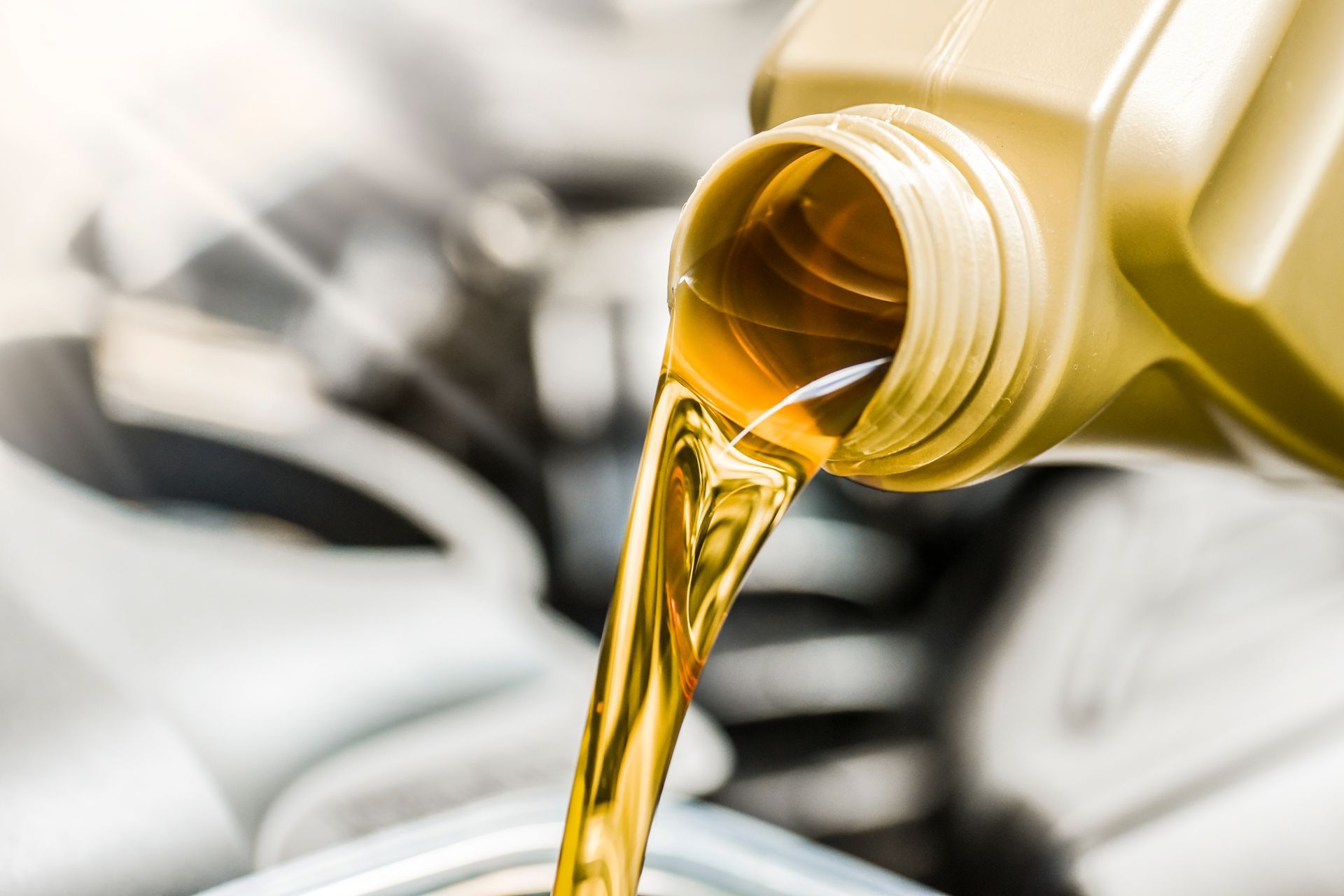 Oil being poured from a yellow container into a car engine.