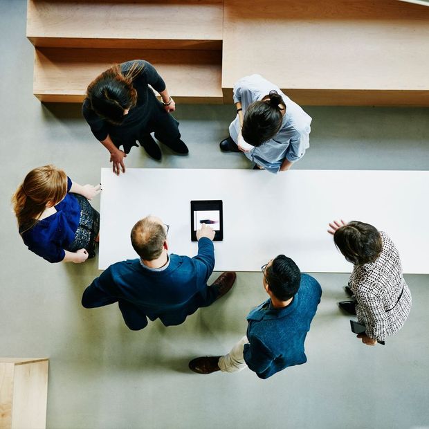 A group of people sitting around a table looking at a tablet A group of people sitting around a table looking at a tablet