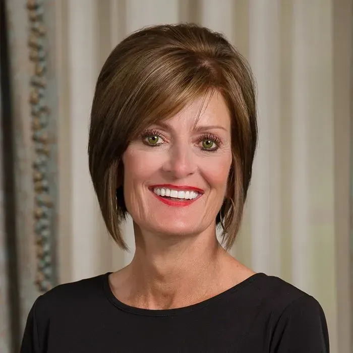 Smiling woman with short brown hair, red lipstick, in front of curtains, wearing a black top.