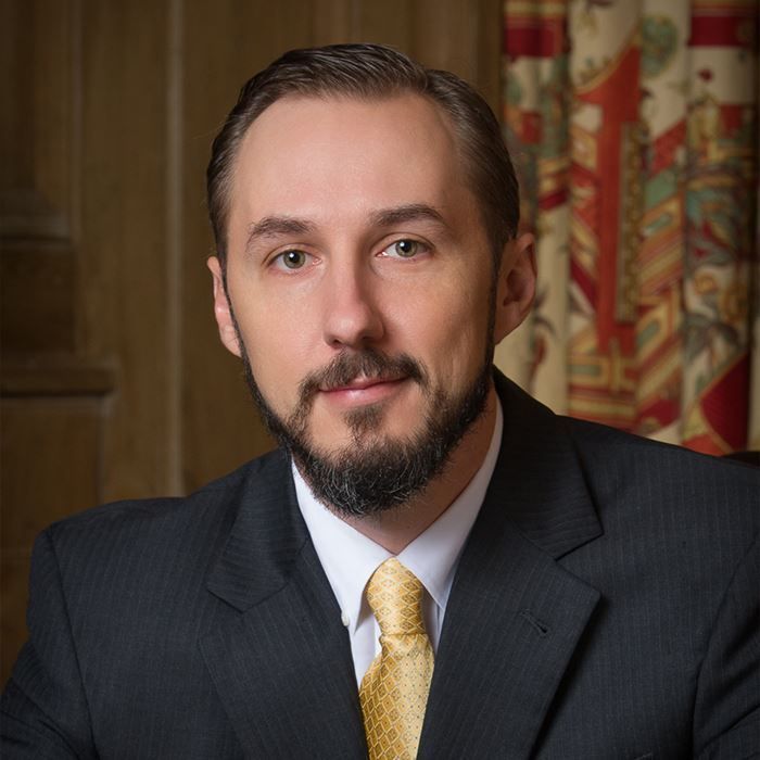 Man in suit with a beard and yellow tie, smiling, in a formal setting.