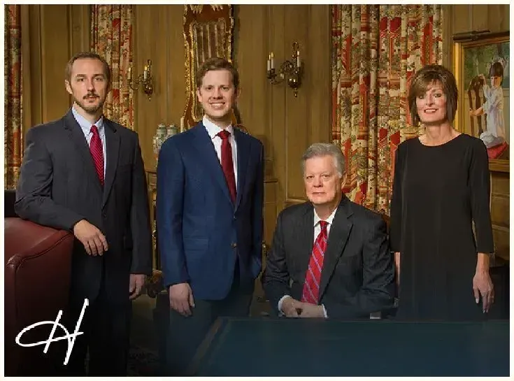 Four people in suits posing for a photo; men in a red tie, woman in black, ornate background.