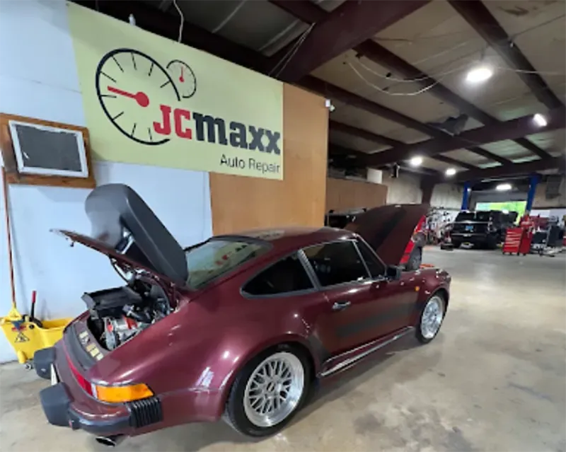 Maroon Porsche in auto repair shop with hood open, next to a JC Maxx sign