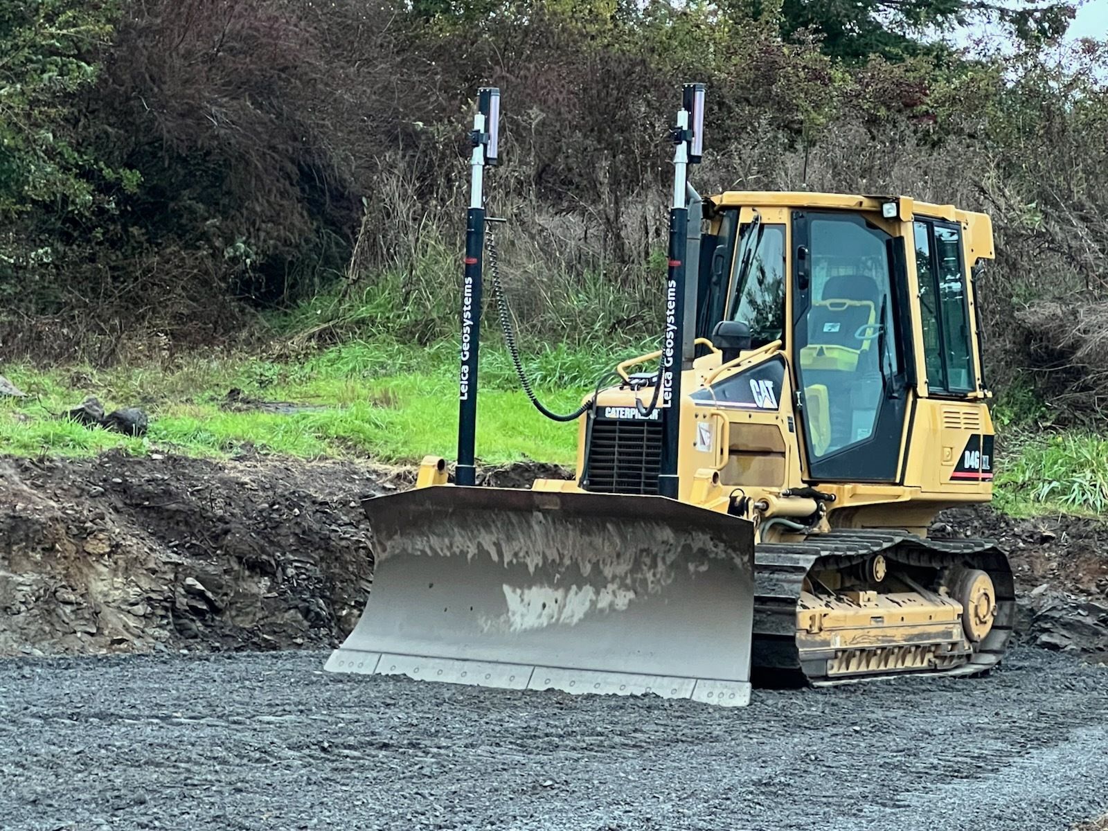 A yellow Caterpillar bulldozer with grade control masts sits on a gravel construction site.