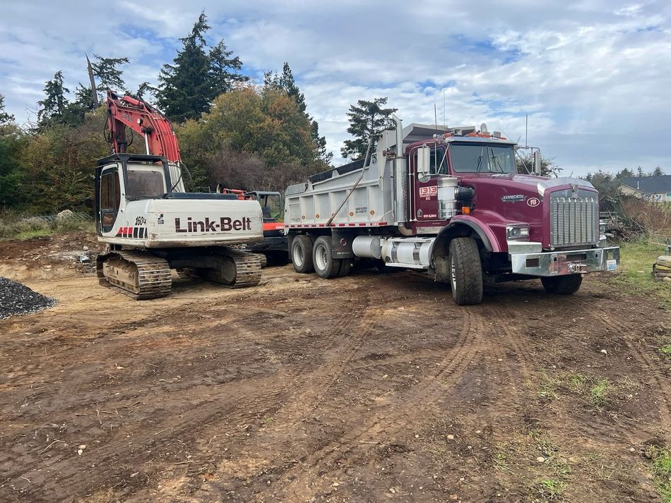 A white Link-Belt excavator parked next to a large maroon and white dump truck on a dirt construction site.