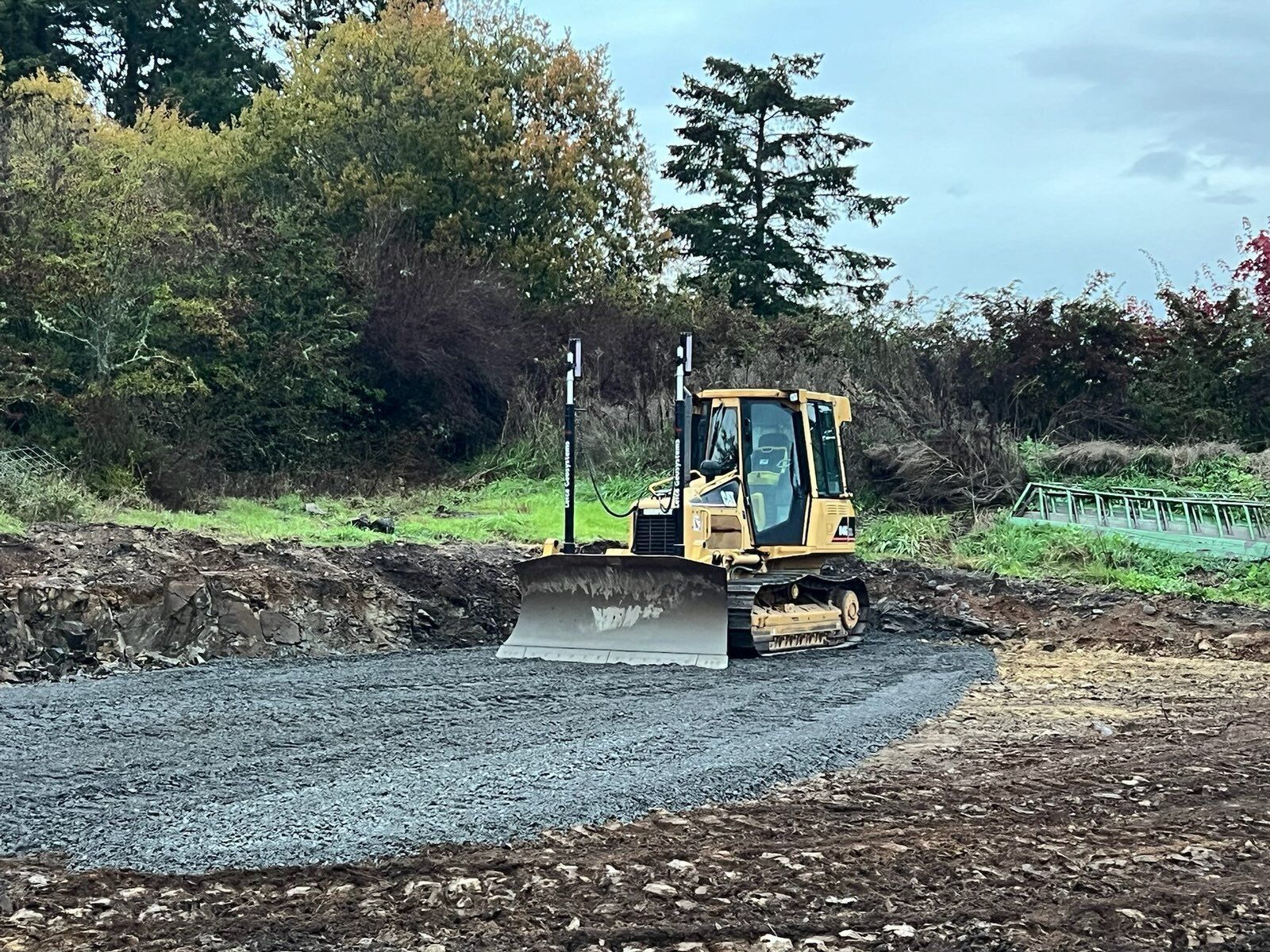 A yellow bulldozer spreads gravel on a construction site with trees in the background.