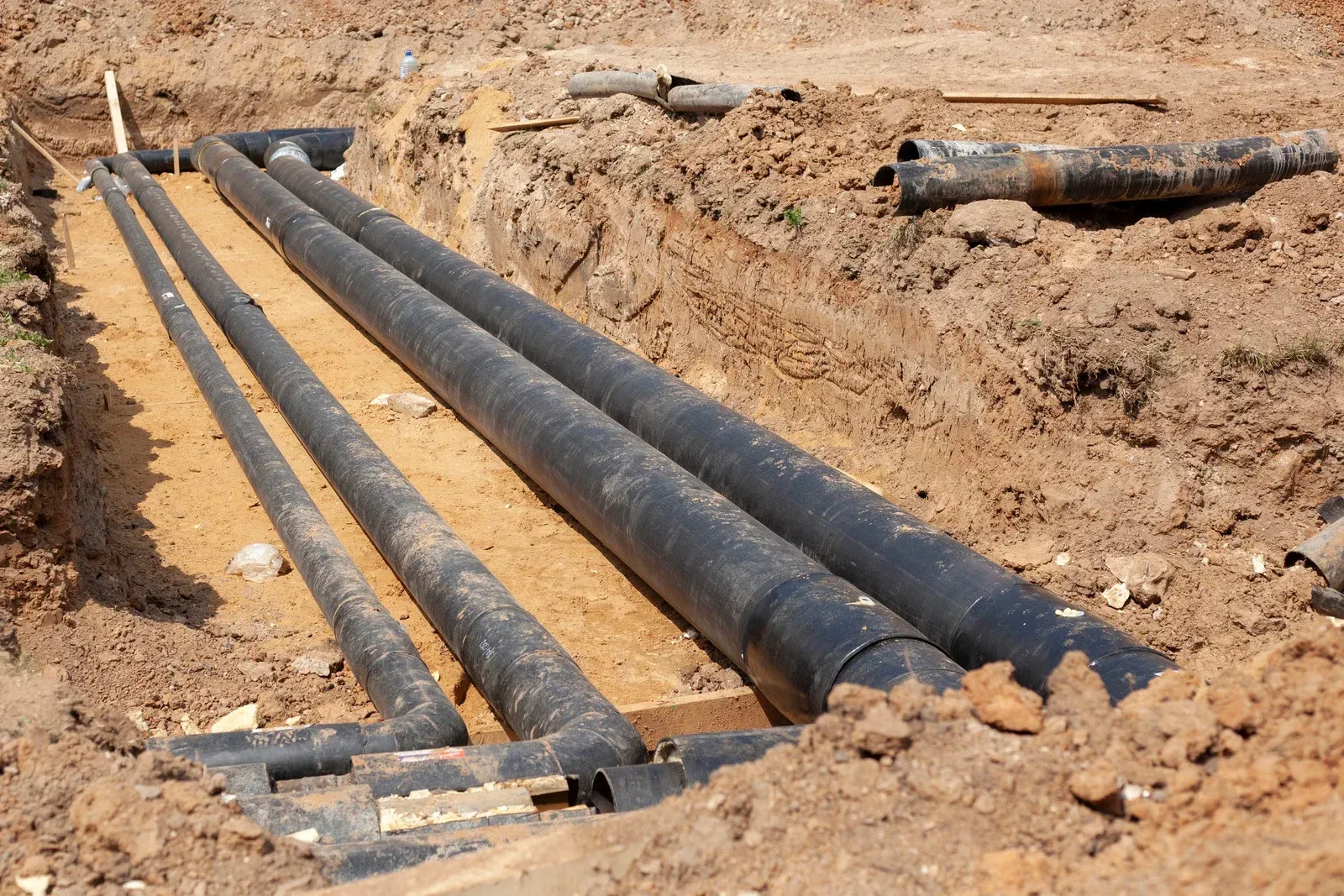Black pipes laid in a narrow, dirt-filled construction trench.