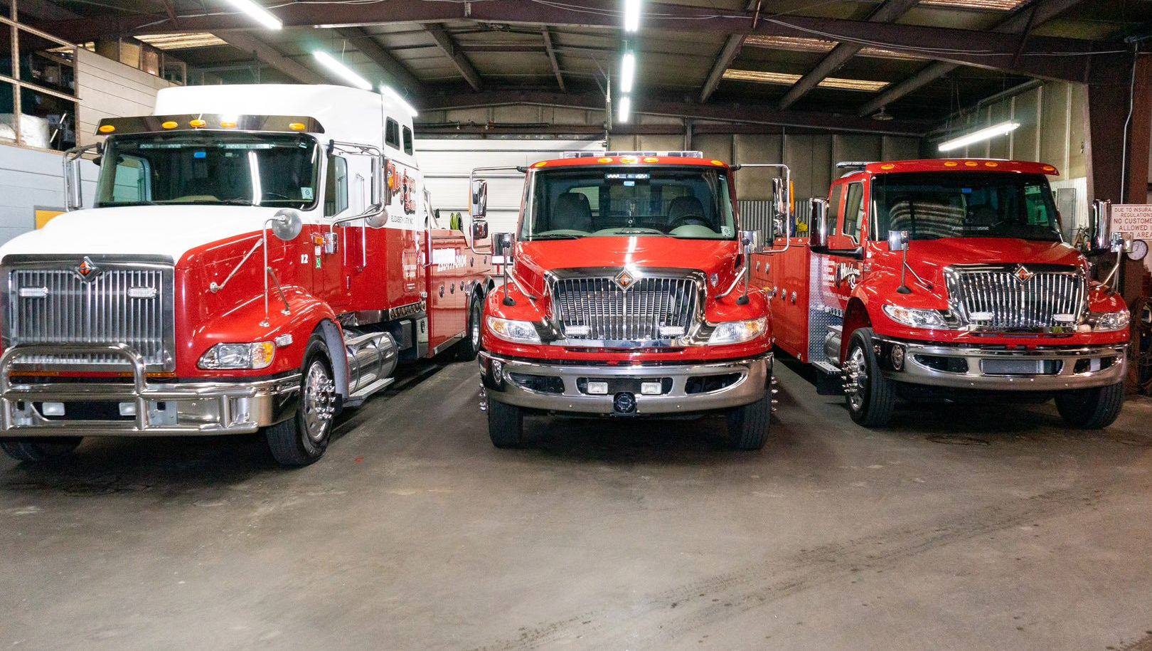 Three red tow trucks parked inside a garage, each with chrome accents.