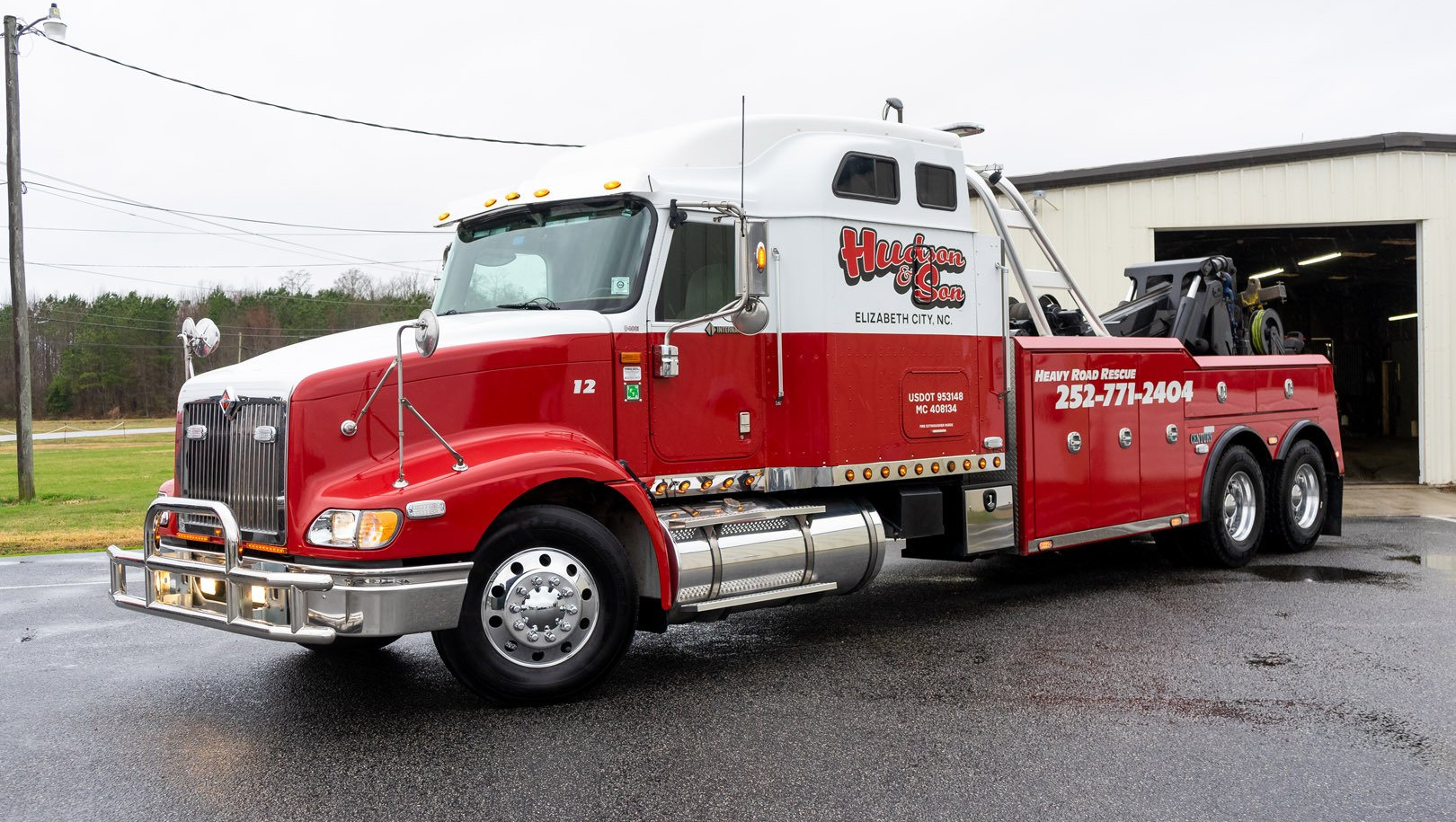 Red and white tow truck with a wrecker. Parked in front of a building.