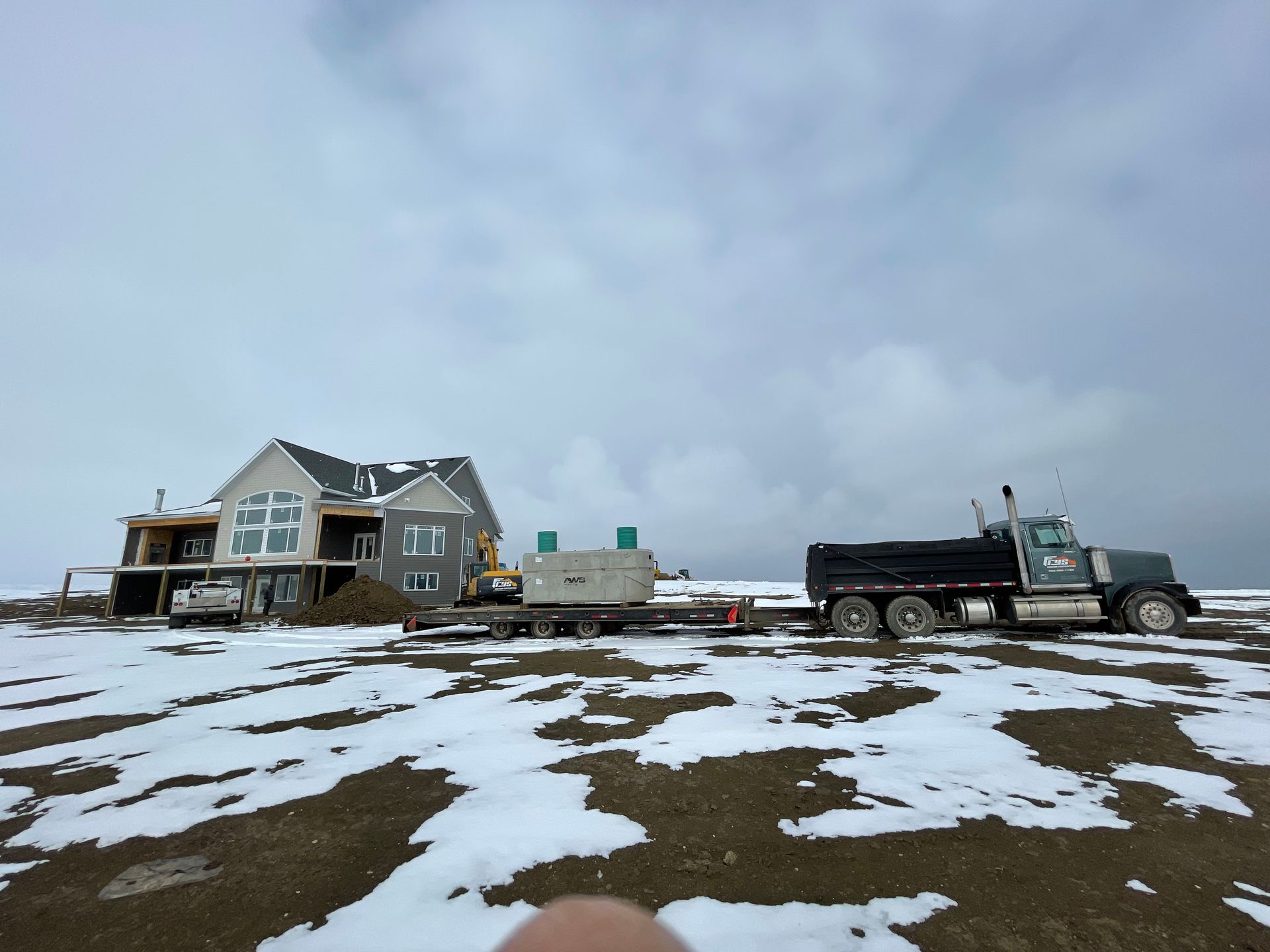 A dump truck is pulling a trailer with a house in the background