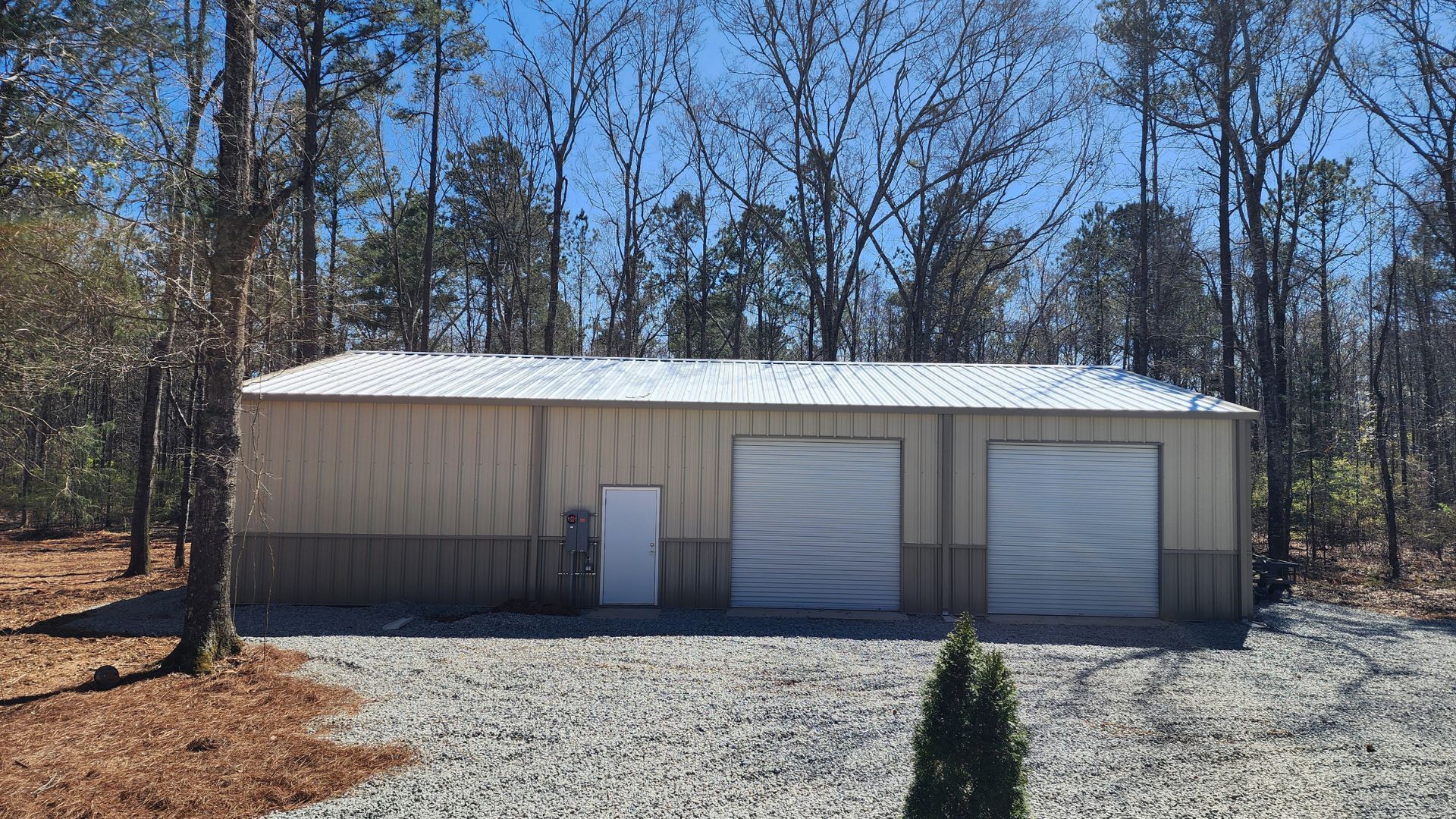 A large metal building with two garage doors is surrounded by trees.