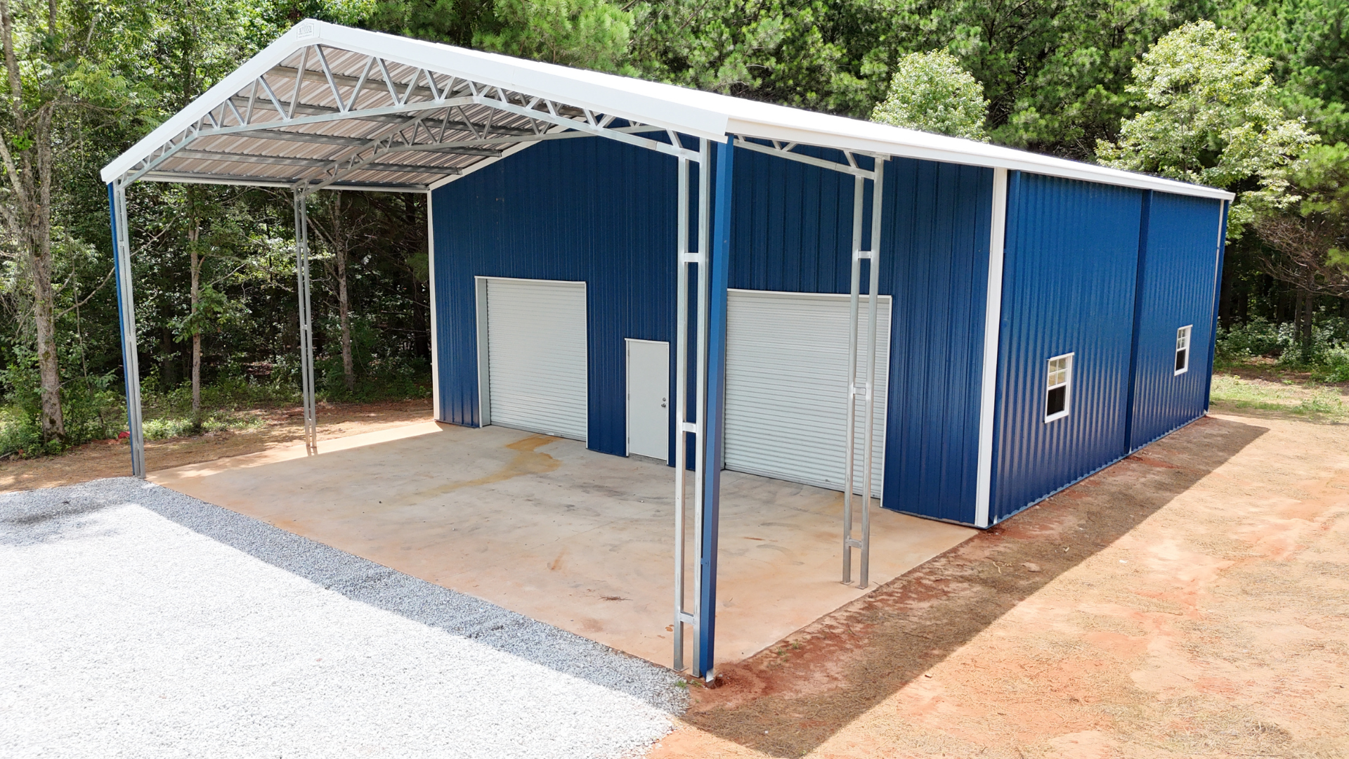 Red metal workshop with garage door and attached carport.